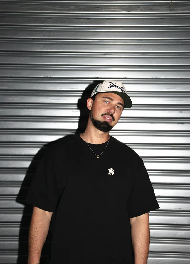 Sonny Fodera in a black cap and T-shirt against a metal shutter